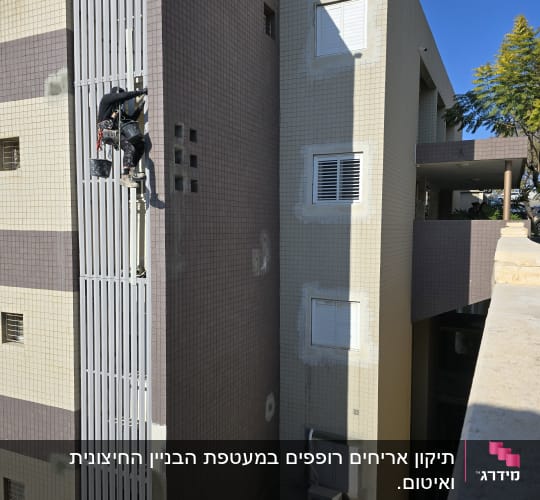 אדם עובד בגובה על בניין עם ציוד בטיחות
